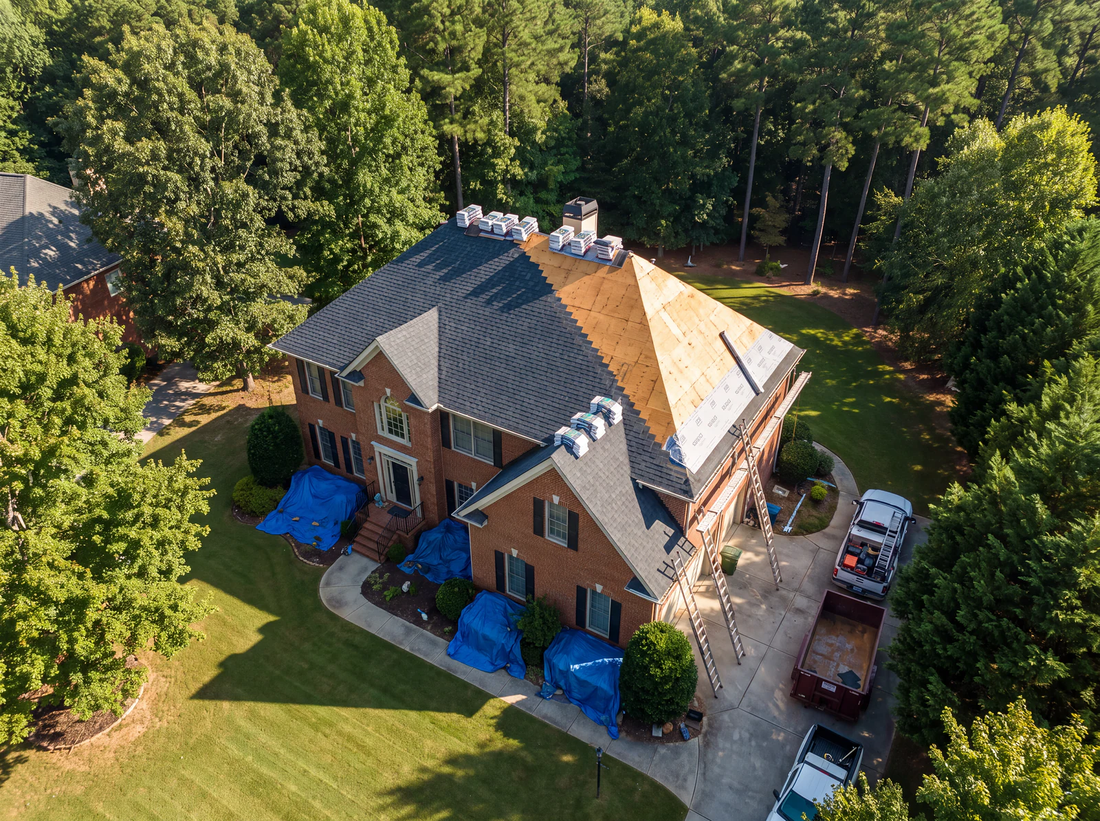 GSP Exterior Works crew mid roof replacement on a brick home, materials staged in the driveway and tarps protecting the landscaping