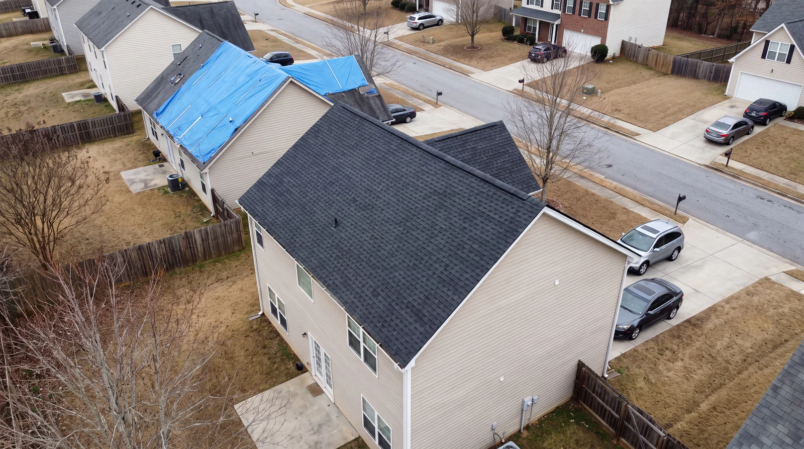 Aerial view of a North Georgia neighborhood after a storm, one home already re roofed and a neighboring roof still covered by a blue tarp